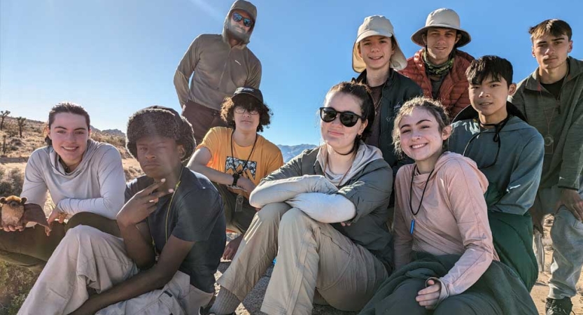 A group of people sit on a rock in a desert environment and smile for the photo. 